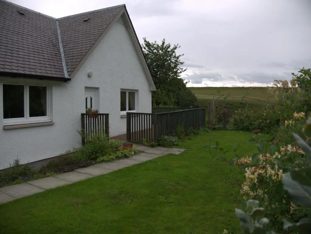 a white house with a fence and a yard at Ornum Cottage in Beauly