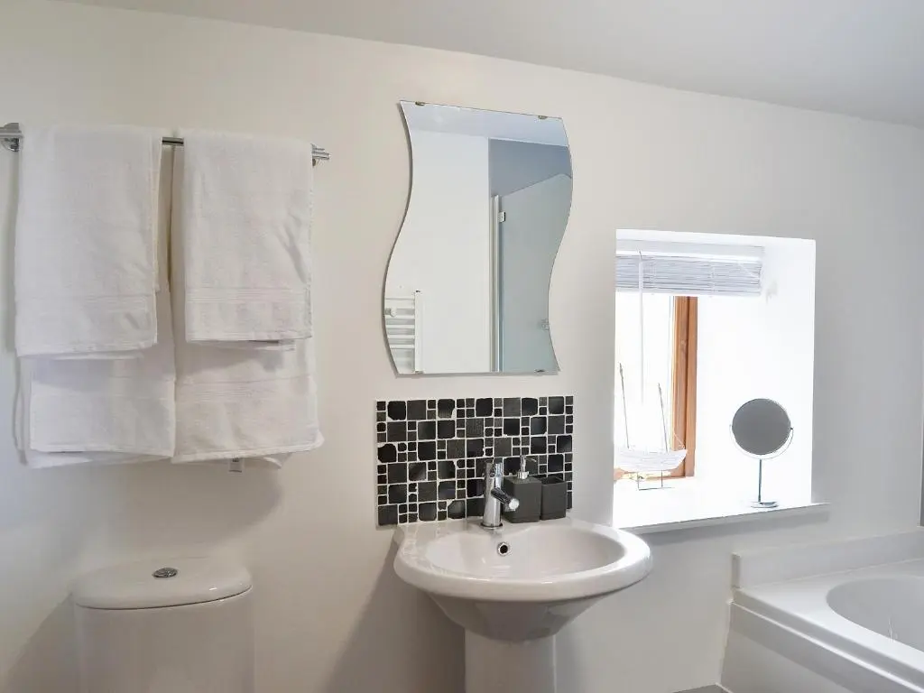 a white bathroom with a sink and a mirror at Sandy's Hoose in Portmahomack