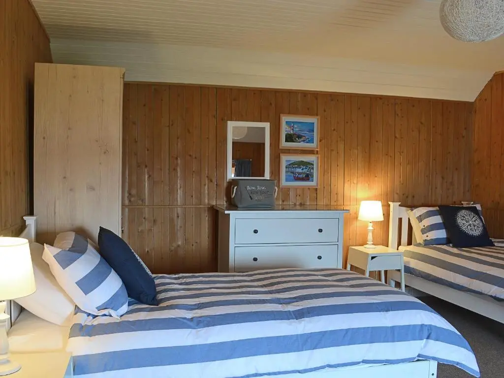 a bedroom with two beds and a dresser and two lamps at Sandy's Hoose in Portmahomack
