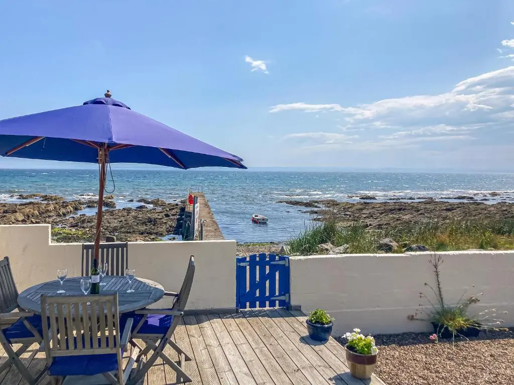 a patio with a table and an umbrella and the ocean at Cross Tides in Hilton of Cadboll