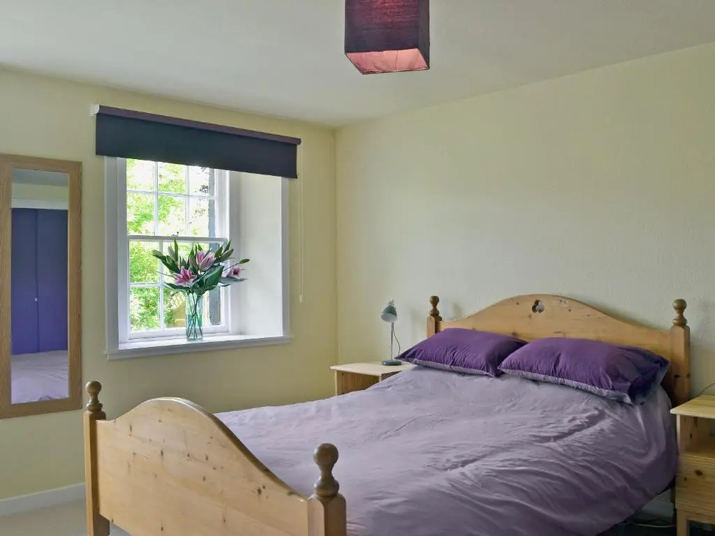 a bedroom with a bed with purple pillows and a window at Kinnettas Cottage in Strathpeffer