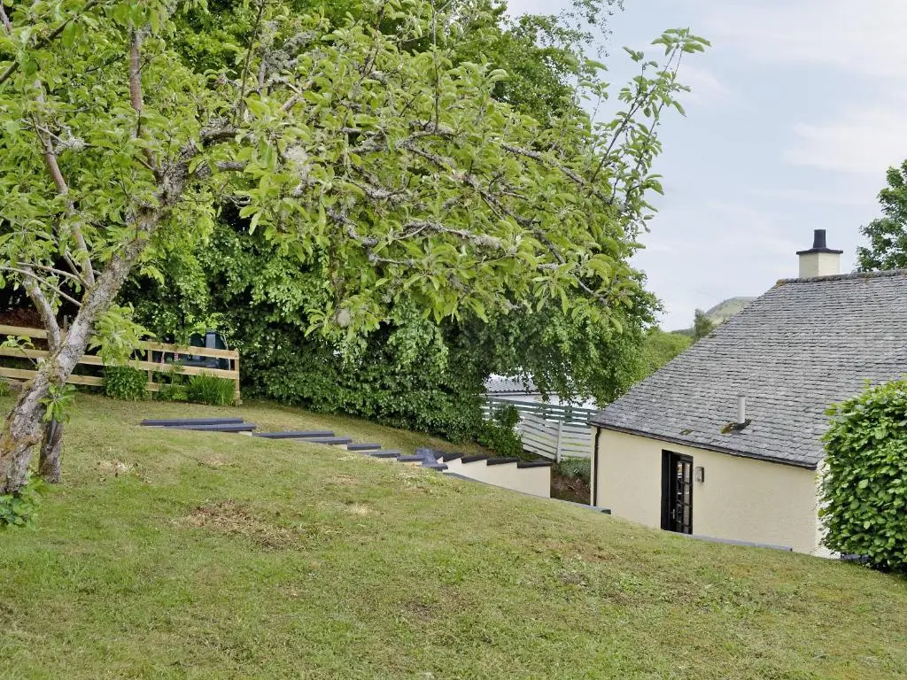 a house on a hill next to a tree at Kinnettas Cottage in Strathpeffer