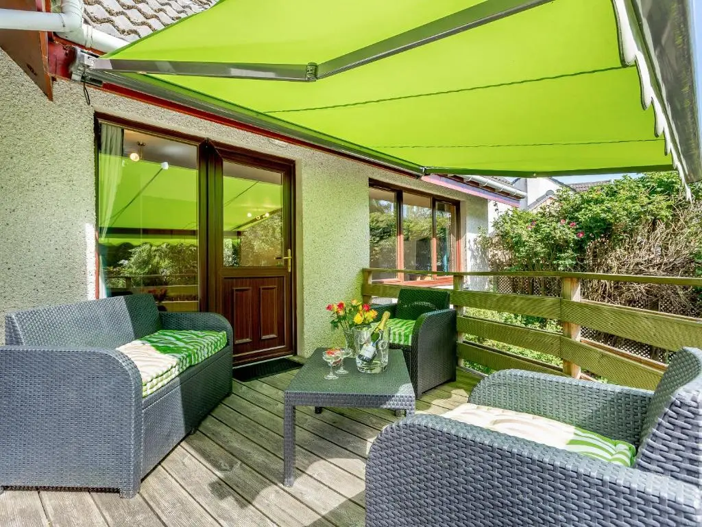a patio with chairs and a table and a green umbrella at Glen View Of Enrick House in Bearnock