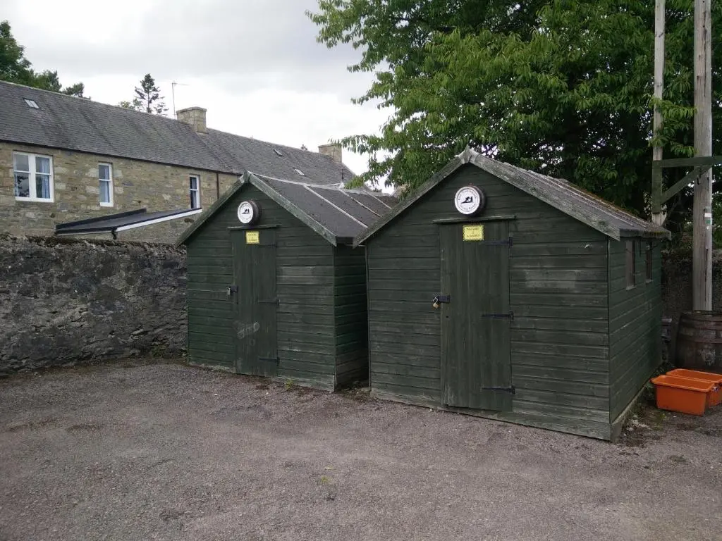 two green storage sheds in a yard next to a building at The Smugglers Hostel in Tomintoul
