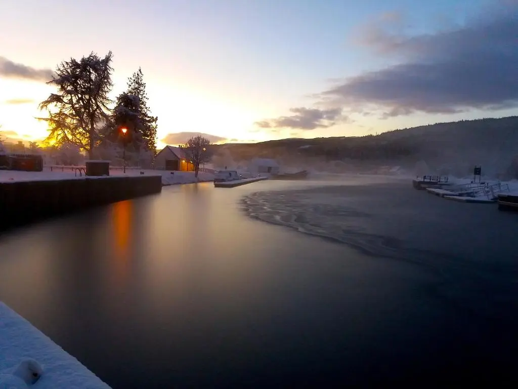 a body of water with the sun setting in the background at Loch Ness Highland Cottages with partial Loch View in Invermoriston