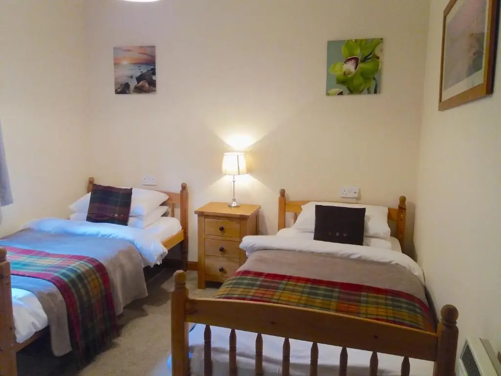 a bedroom with two beds and a night stand with a lamp at Loch Ness Highland Cottages with partial Loch View in Invermoriston