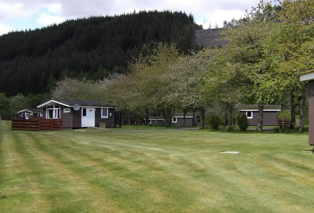 a large yard with two houses and a hill at Forest Glen Holiday Park in Invermoriston