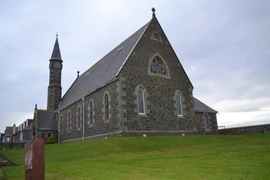a church with a clock tower on a grass field at Belvedere Holiday Home in Whitehills