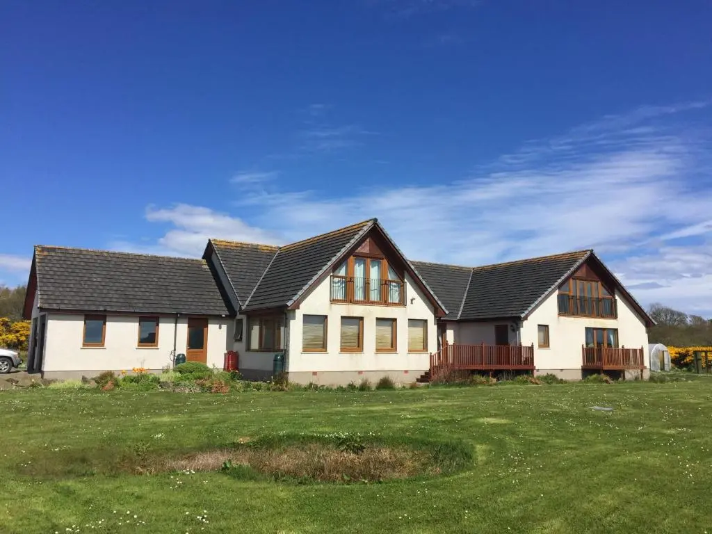 a white house with a black roof on a green field at Acarsaid B&B in Lybster