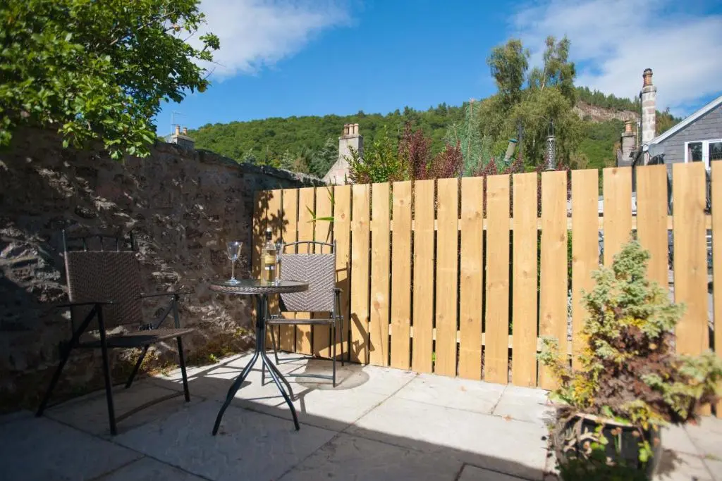 a patio with two chairs and a table and a fence at Glenernan Self Catering Cottages in Ballater