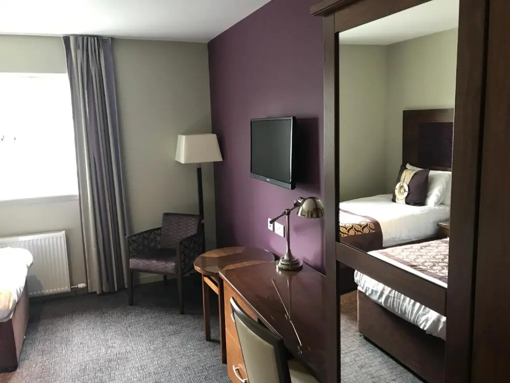 a hotel room with a bed and a desk with a mirror at Buchan Hotel in Ellon