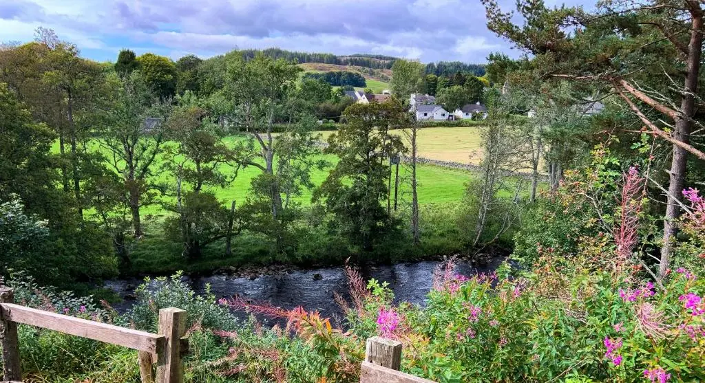 a view of a garden with a river and flowers at Strathardle Lodge in Kirkmichael