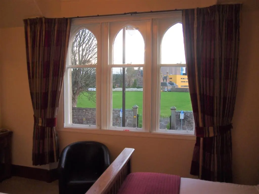 a bedroom with two windows and a bed and a chair at Craignay Guest House in Inverness