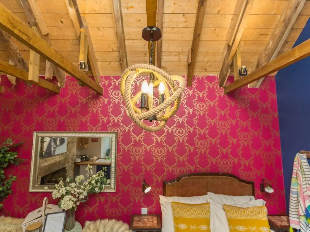 a bedroom with a pink wall with a mirror and a chandelier at Glamping Bothie in Inverurie