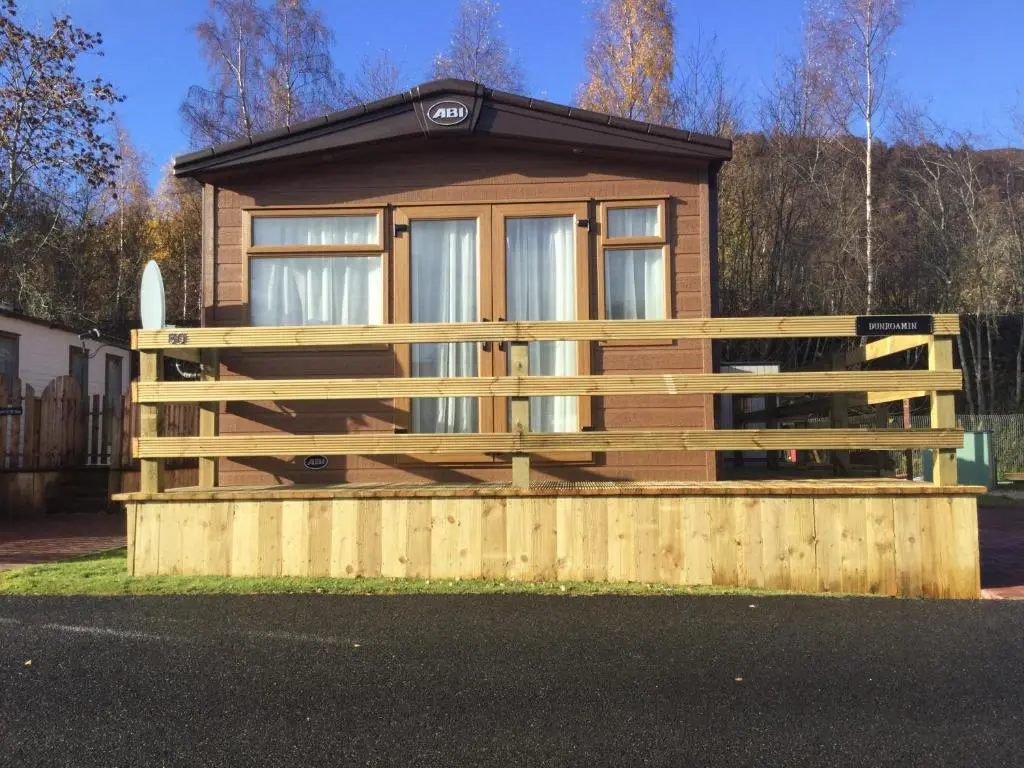 a wooden house with a fence in front of it at Dunroamin Lodge in Aviemore
