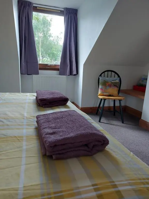 a bedroom with a bed and a chair and a window at Holiday House Kinveachy in Aviemore