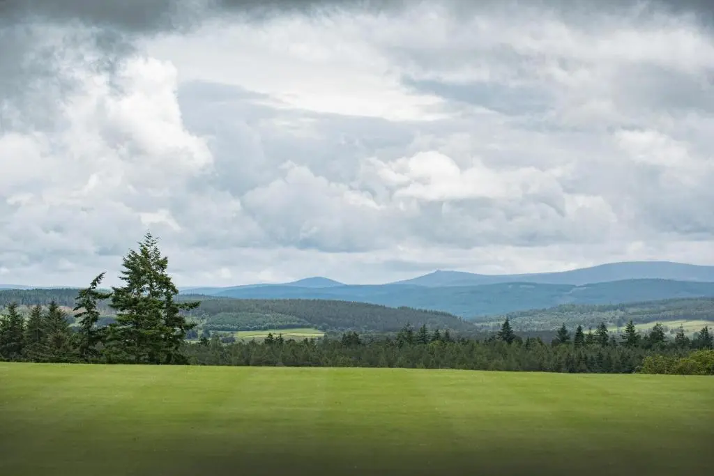 a green field with trees and mountains in the background at Douneside House in Tarland