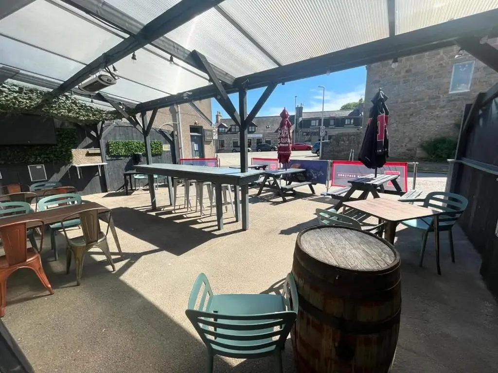 a patio with tables and chairs and a barrel at The Square Kintore in Kintore