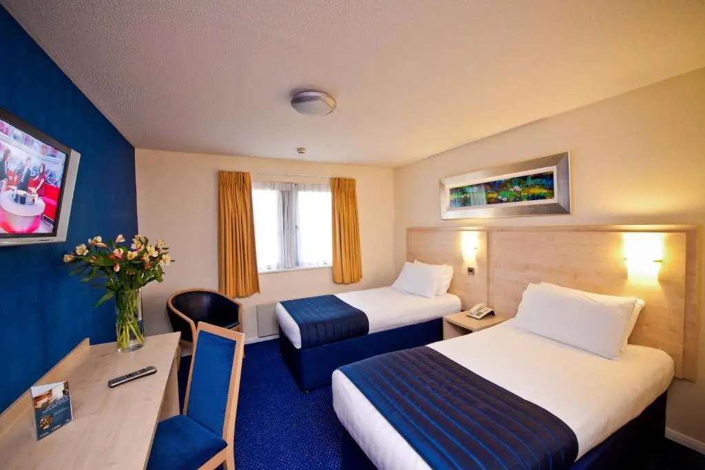 a hotel room with two beds and a desk at Leonardo Inn Aberdeen Airport in Dyce