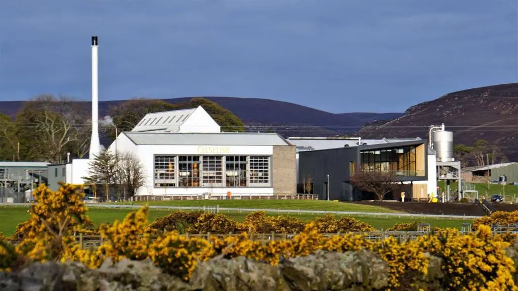 a large white building with flowers in front of it at Auchencairn Cottage in Brora