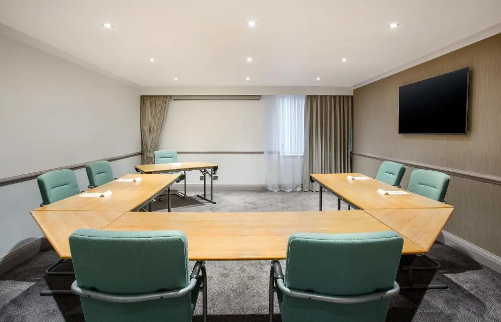 a conference room with wooden tables and green chairs at Leonardo Hotel and Conference Venue Aberdeen Airport in Dyce
