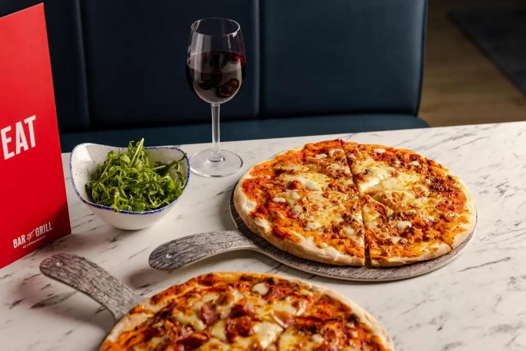two pizzas sitting on a table with a glass of wine at Leonardo Hotel Inverness in Inverness