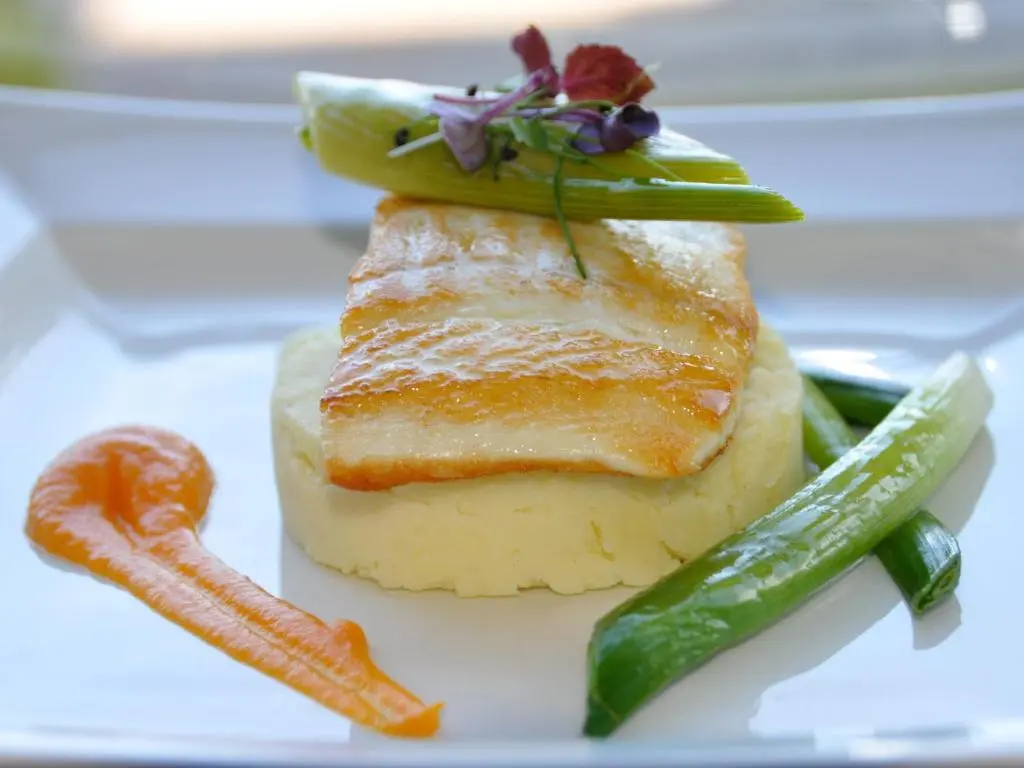 a piece of fish on a white plate with vegetables at Macdonald Drumossie Hotel Inverness in Inverness