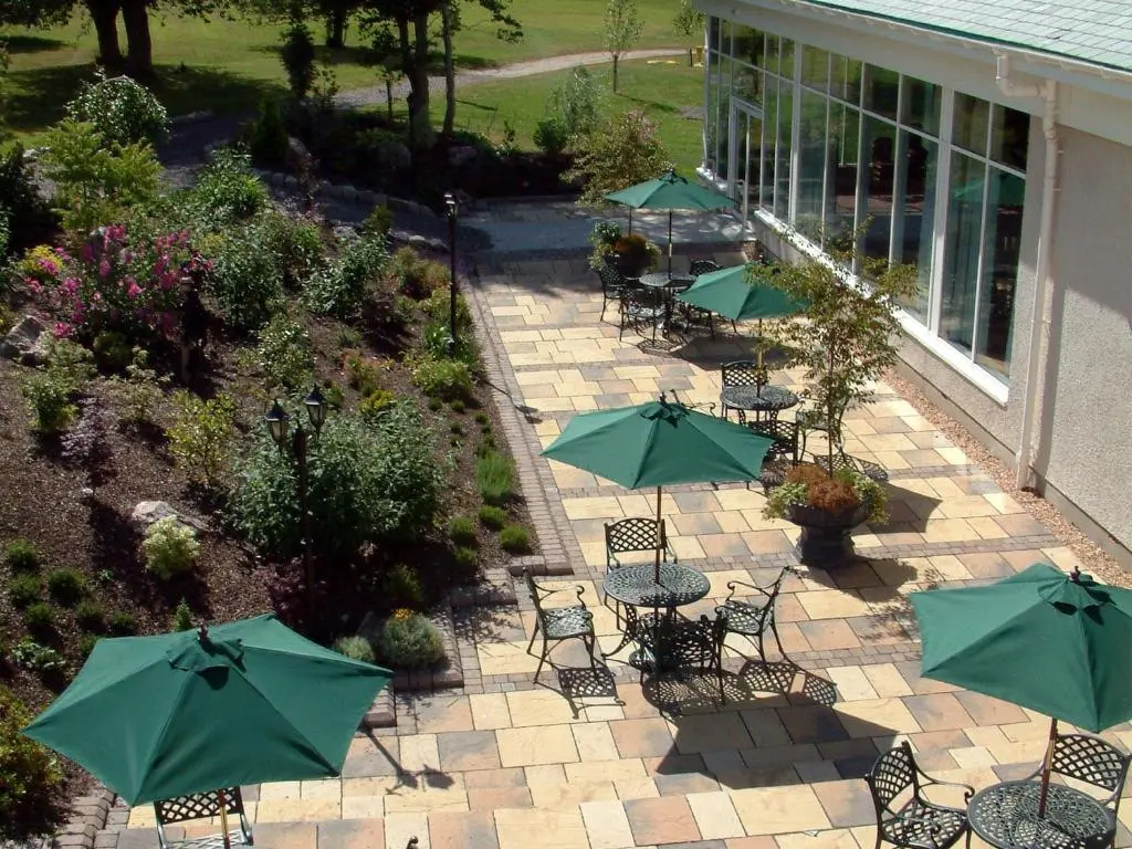 a patio with tables and chairs with green umbrellas at Macdonald Drumossie Hotel Inverness in Inverness