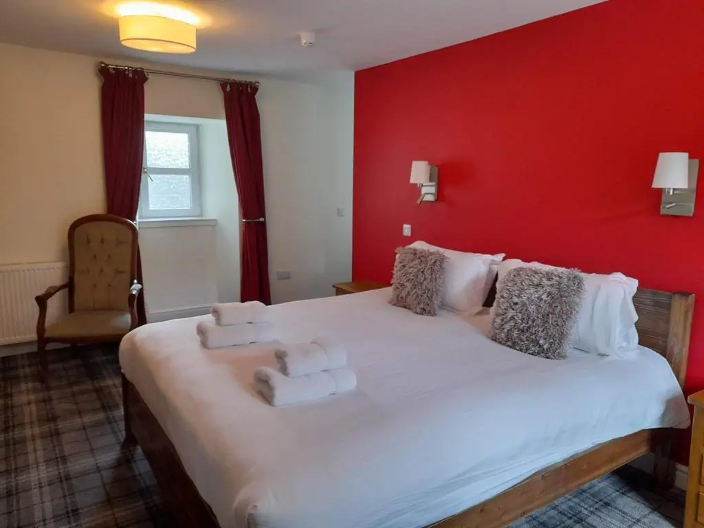 a bedroom with a large white bed with a red wall at The Rowan Tree Country Hotel in Aviemore