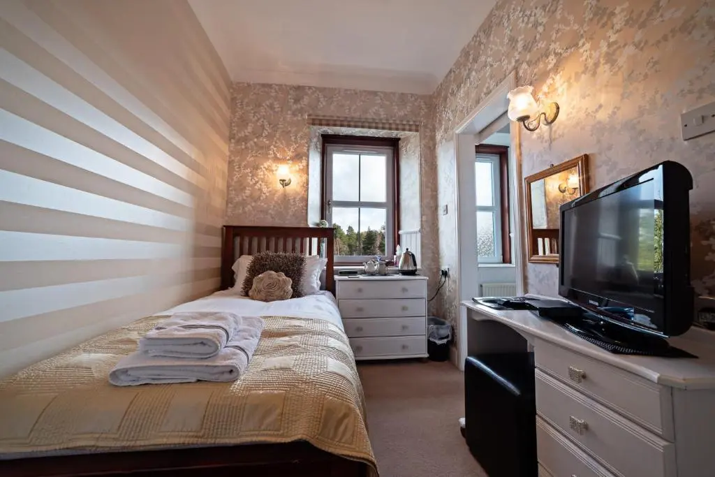 a bedroom with a bed with a television and a desk at The Rowan Tree Country Hotel in Aviemore