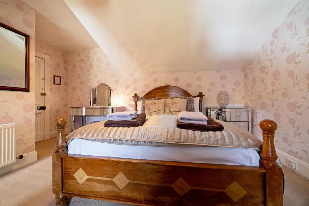a bedroom with a wooden bed with pink wallpaper at The Rowan Tree Country Hotel in Aviemore
