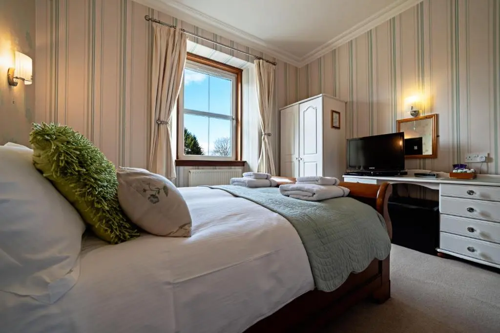 a bedroom with a bed with a desk and a television at The Rowan Tree Country Hotel in Aviemore