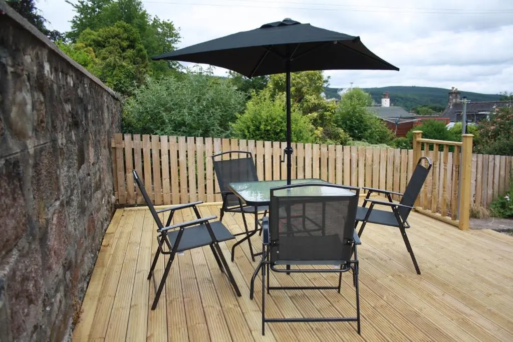 a table and chairs with an umbrella on a deck at Mary's Apartment in Rothes