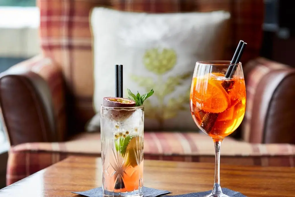 two cocktails on a wooden table with a drink at Macdonald Highlands Hotel at Macdonald Aviemore Resort in Aviemore
