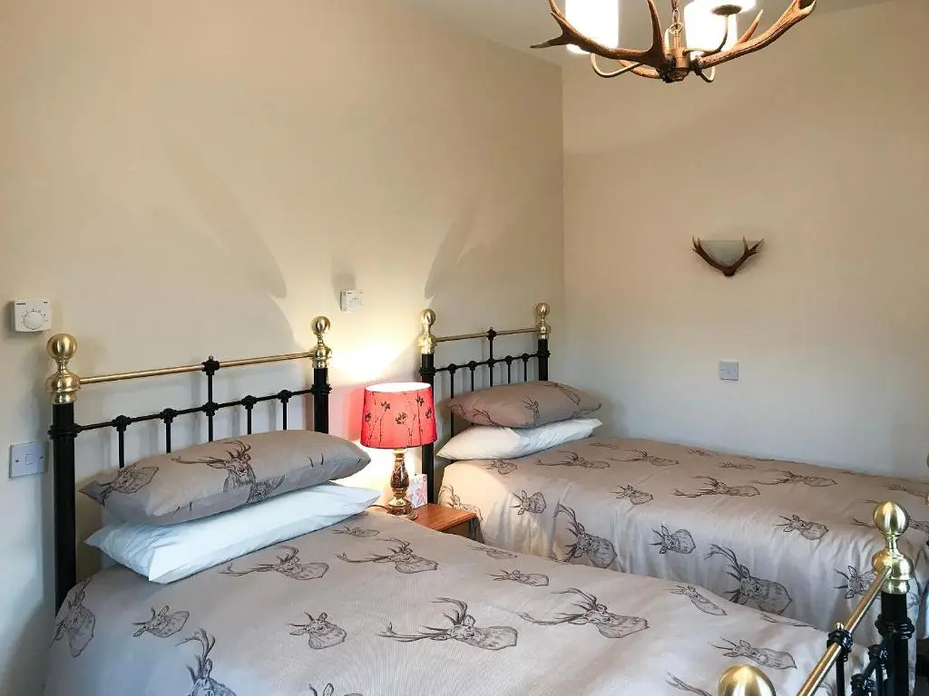 two beds in a room with a lamp on a table at Turin Nurin Cottage in Tomatin