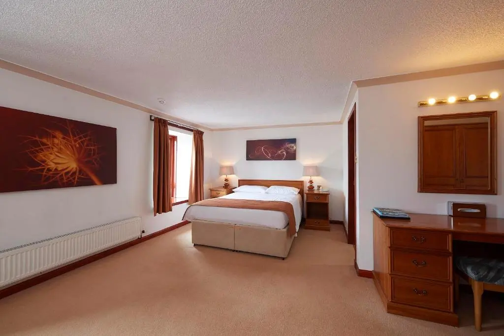 a bedroom with a bed and a desk and a window at The Priory Hotel in Beauly