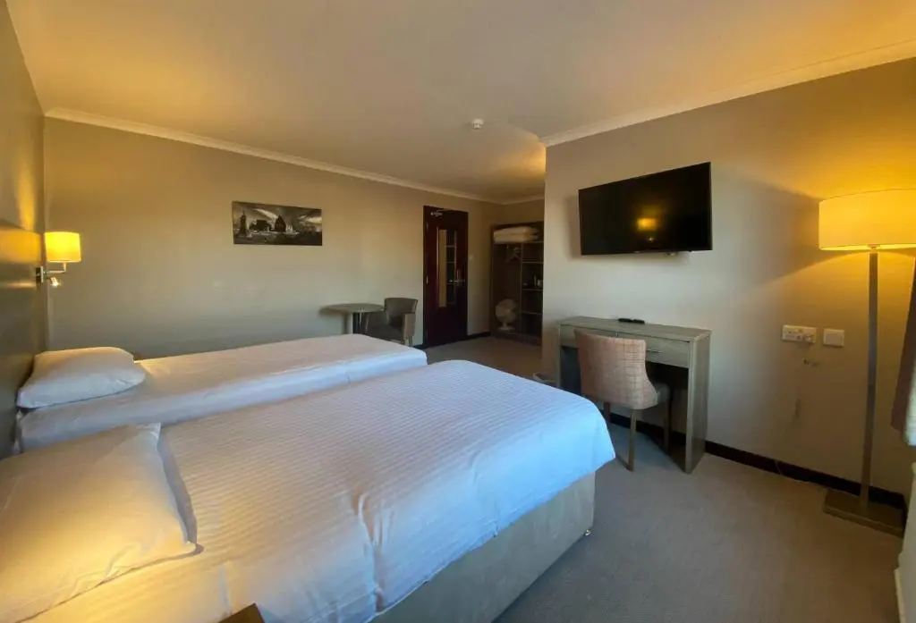 a hotel room with two beds and a desk and a television at The Priory Hotel in Beauly