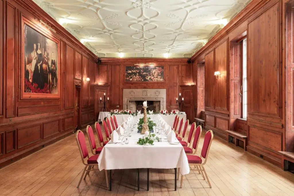 a long table in a room with red chairs at Tulloch Castle Hotel \u2018A Bespoke Hotel\u2019 in Dingwall