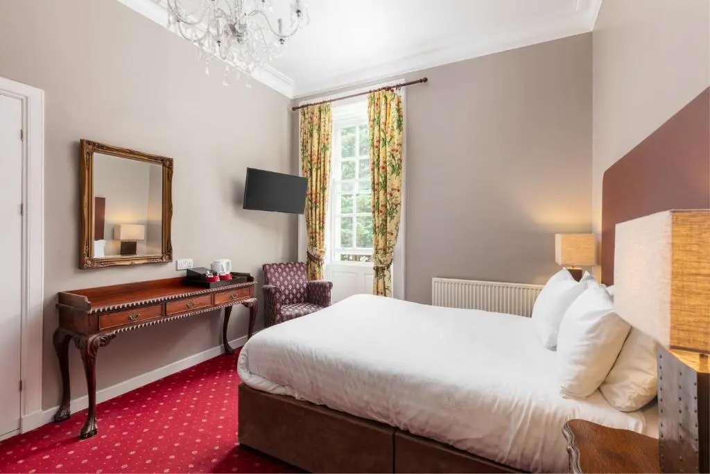 a bedroom with a bed and a desk and a mirror at Tulloch Castle Hotel \u2018A Bespoke Hotel\u2019 in Dingwall