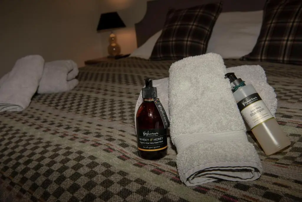 a bottle of alcohol and towels on a bed at Albatross B&B Dornoch in Dornoch