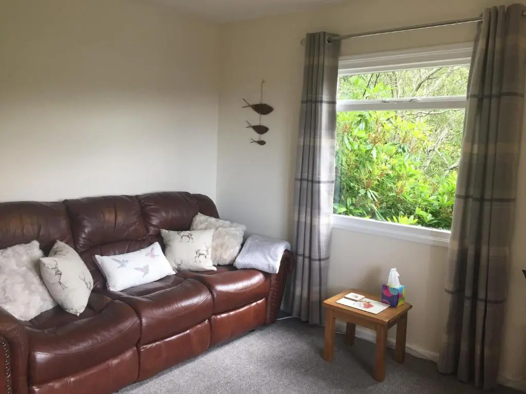 a brown leather couch in a living room with a window at Loch Broom Cabins Seaviews& Petfriendly in Leckmelm