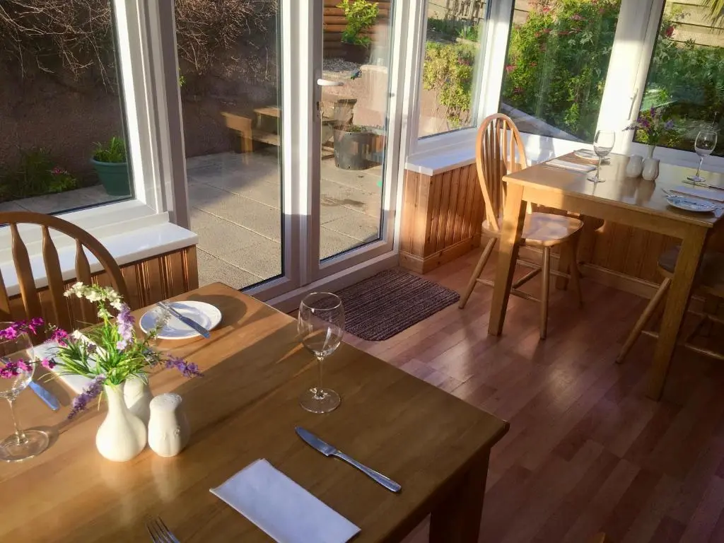 a dining room with a table and chairs and windows at White Cottage B&B in North Kessock