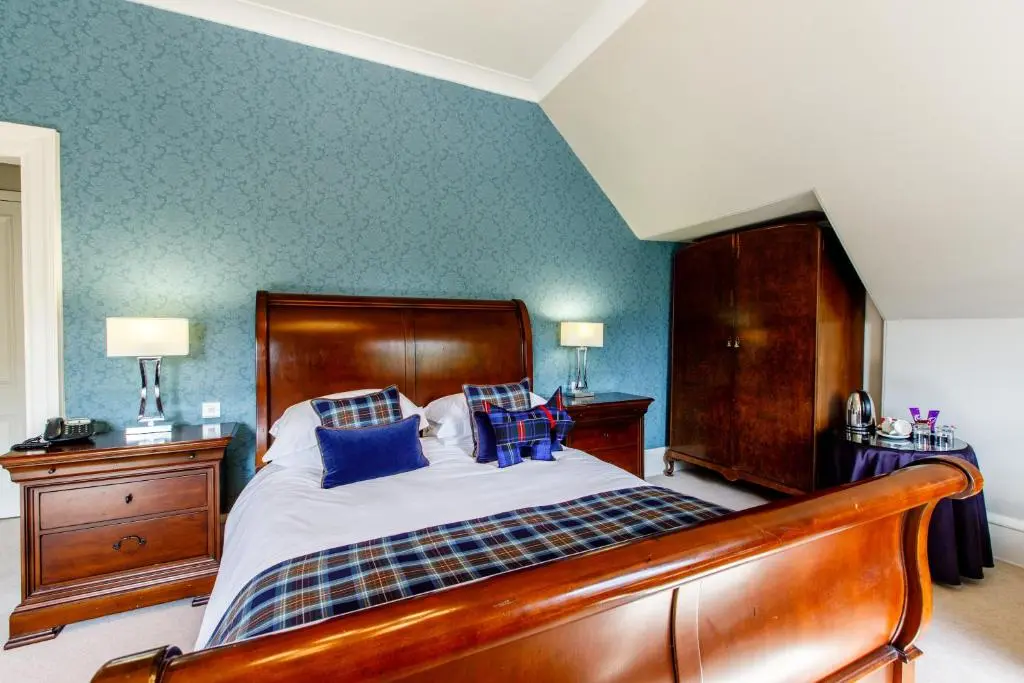 a bedroom with a wooden bed with blue walls at Tor-Na-Coille Hotel in Banchory