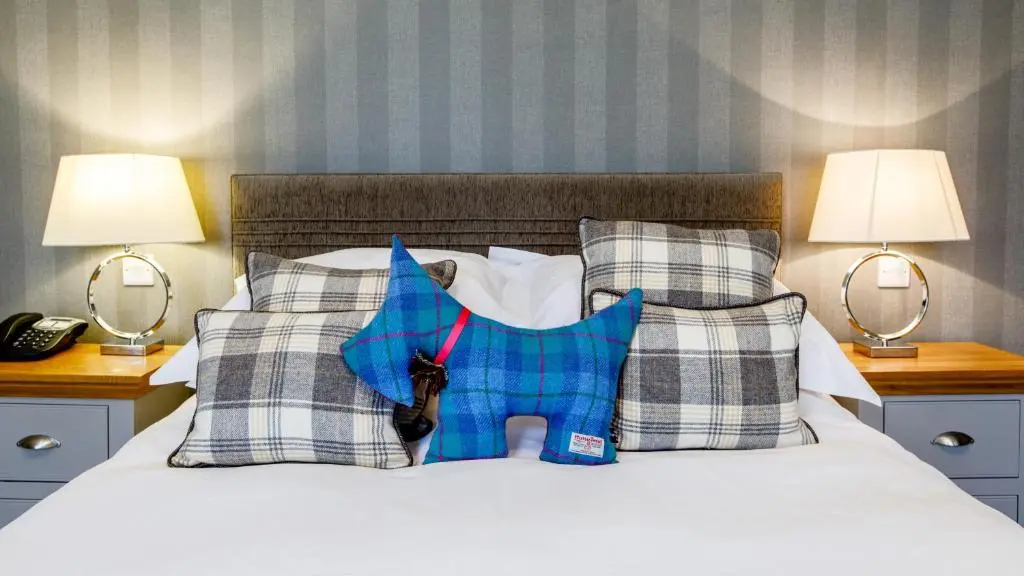 a blue dog pillow on a bed with two lamps at Tor-Na-Coille Hotel in Banchory