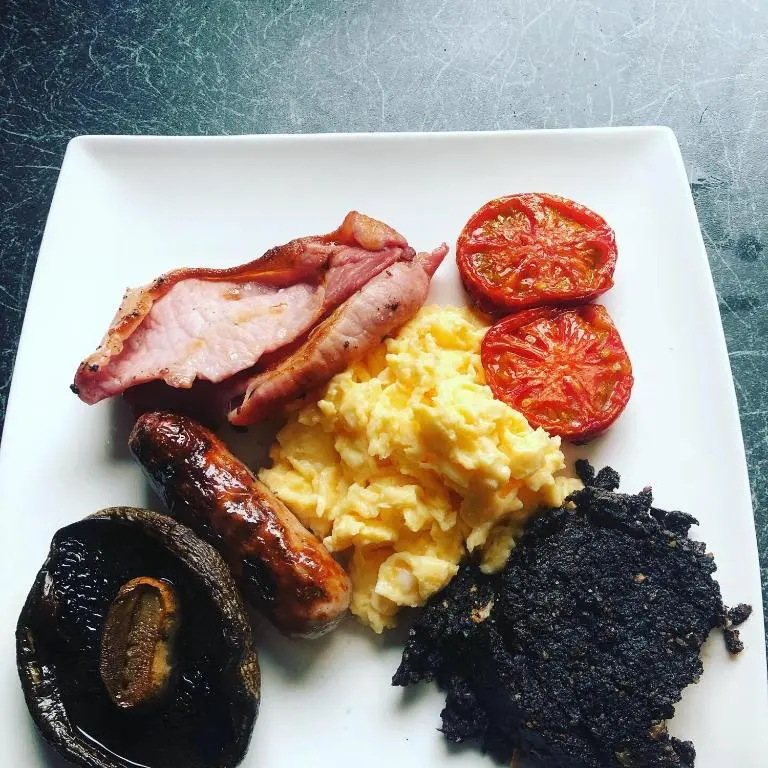 a plate of breakfast food with eggs bacon and tomatoes at Strathallan B&B in Inverness
