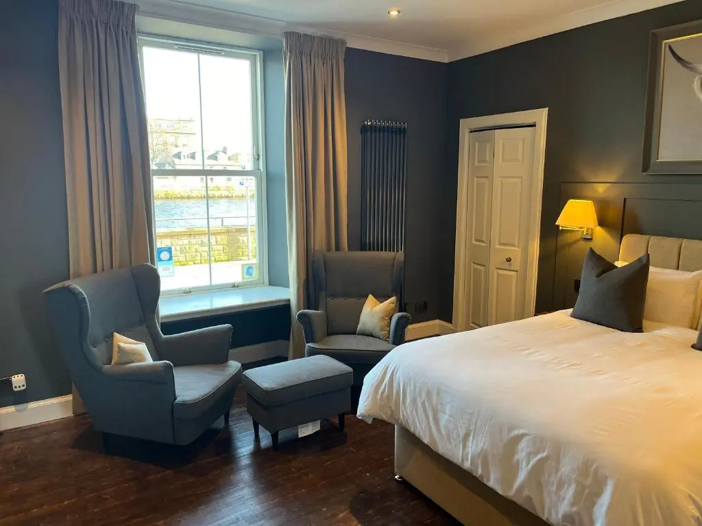 a bedroom with a bed and two chairs and a window at Fraser House in Inverness