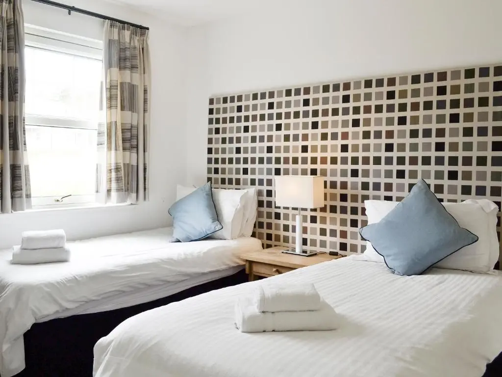 two beds in a room with a window and a couch at 22 Queens Court in Inchmarlo