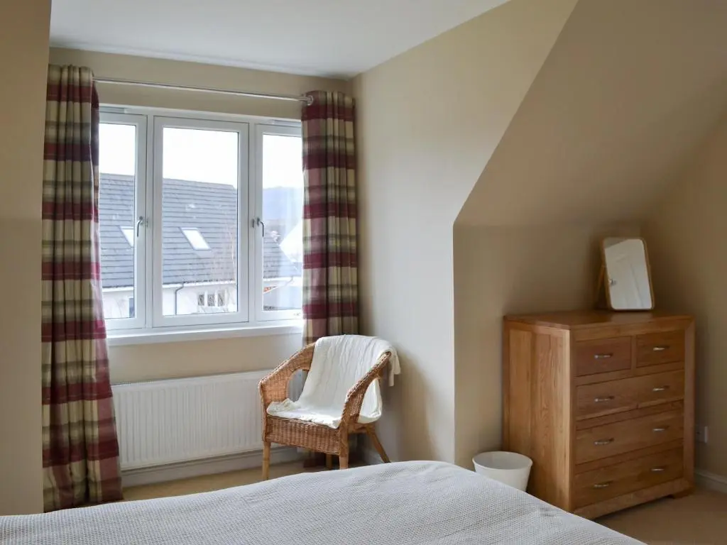 a bedroom with a bed and a dresser and a window at Stags Neuk in Aviemore