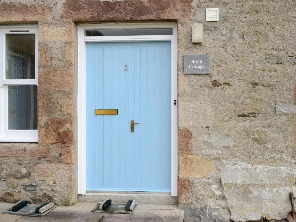 a blue door on the side of a stone building at Birch Cottage in Glenrossal