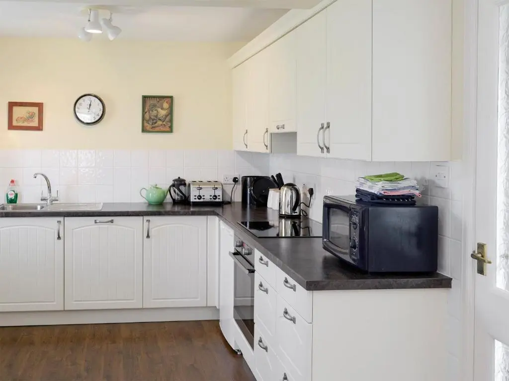 a kitchen with white cabinets and a microwave at Rowan Cottage in Glenrossal
